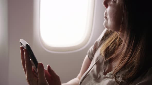Closeup of woman using cell phone on airplane
