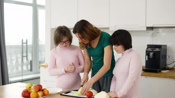 Two Girls with Down Syndrome are Learning to Cook with Their Mother in Kitchen at Home with Fun and alt