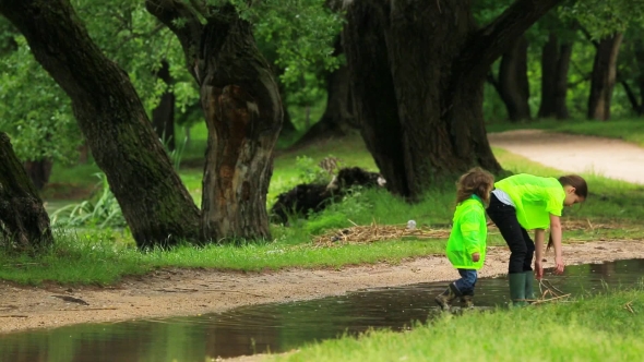 Two Children Walking In Puddle In Park