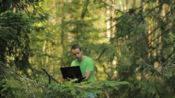 A Man Walks Through The Forest With a Laptop And Looking Map He Chooses The Right Direction