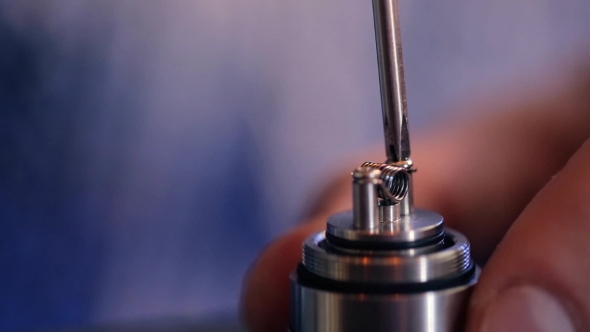 Hand With a Screwdriver, Unscrews Screws Holding Wire Heating Element In Electronic Cigarette. alt