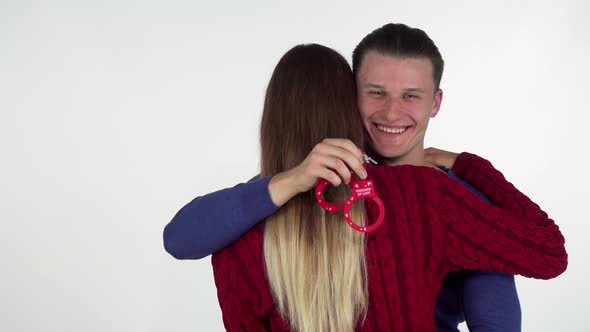 Handsome Man Hugging His Girlfriend, Holding Sex Toy Handcuffs Behind Her Back alt