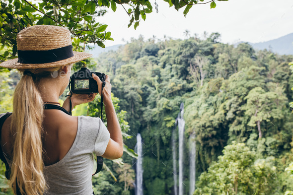 Female tourist photographing a waterfall in forest - Stock Photo - Images