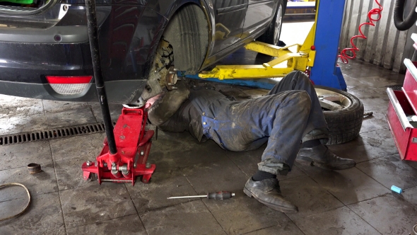 Mechanic Lying And Working Under Car At Repair Garage