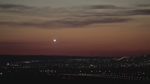 Jet Plane Landing In Silhouette Against An Orange Sunset.