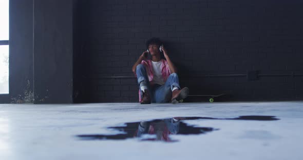 African american man wearing headphones listening to music while sitting in empty parking garage alt