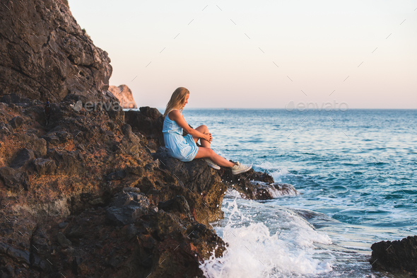 Young blond woman tourist in blue dress relaxing on stone rocks - Stock Photo - Images