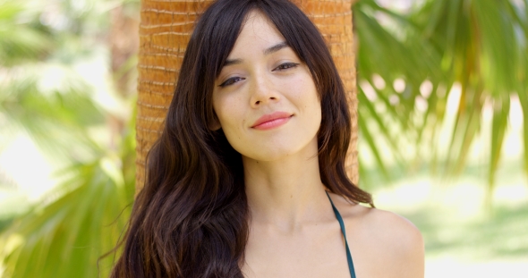 Smiling Young Woman Leaning Against a Palm alt