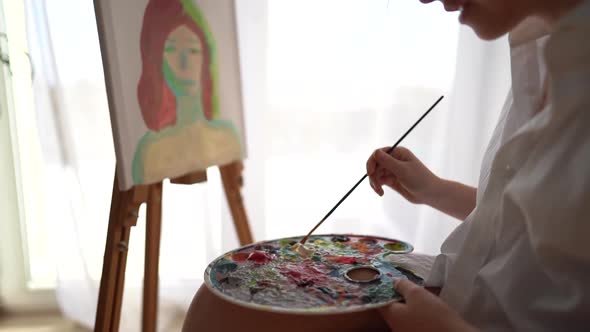 Closeup of a Girl Draws on Canvas with Oil Paints Stirring Them on a Palette alt