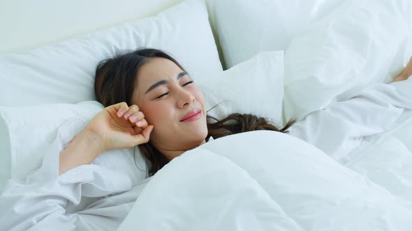 Attractive young woman lying down on bed feel happy with cozy pillow and blanket enjoy early morning alt
