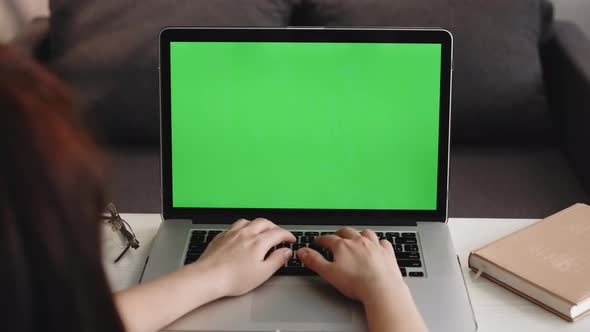Woman Uses Laptop with Green Mock-up Screen While Sitting at the Desk in His Cozy Living Room