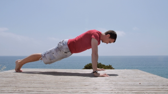 Athletic Caucasian Man Performs Pushups On Rocky Coast Beach On Sunny Day