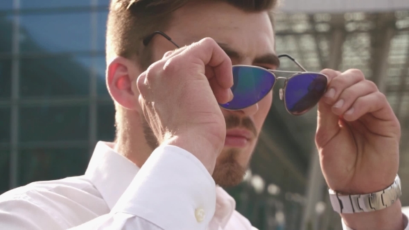 Handsome Fashion Male Model Taking Off His Sunglasses And Looks To The Camera. Urban City Background