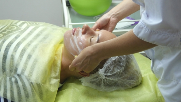 Beautician Applying Facial Mask On a Beautiful Girl Face At Beauty Salon. Woman Having a Facial Care alt