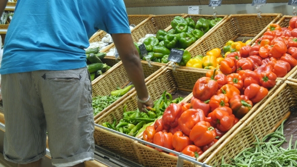 Indian Man Is Choosing Peppers In a Grocery Supermarket. Guy Selecting Fresh Ripe Green Peppers In alt