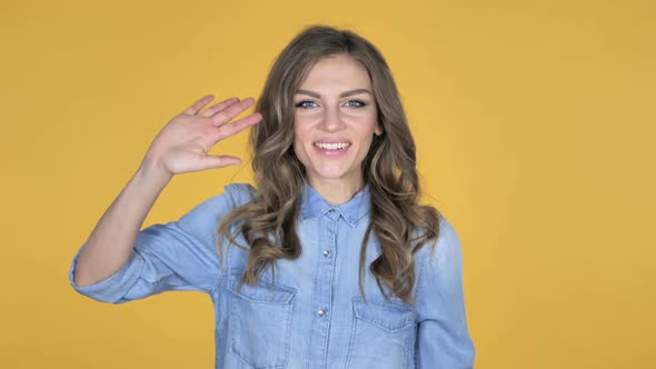 Young Girl Waving Hand to Welcome Isolated on Yellow Background alt