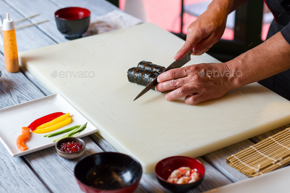 Hand with knife cutting sushi