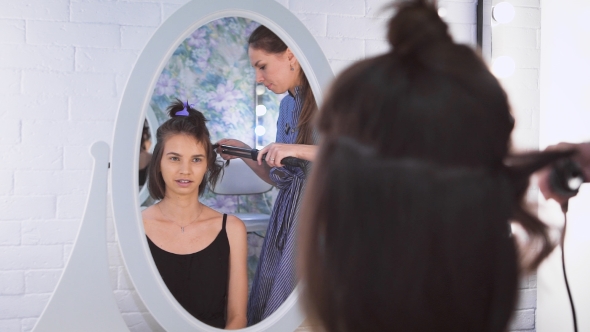 A Beautiful Woman Looking At a Mirrow While a Stylist Is Making Her Hair.