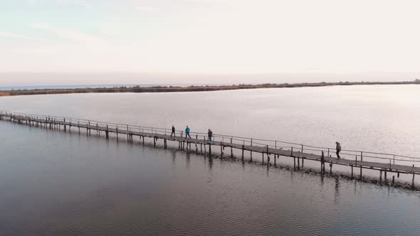People walking on wooden old bridge through estuary with tranquil water surface alt