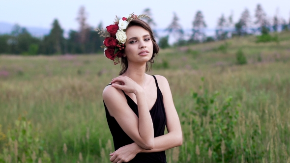 Beautiful Girl In The Black Short Dress With The Wreath On Her Head On The Green Field. alt