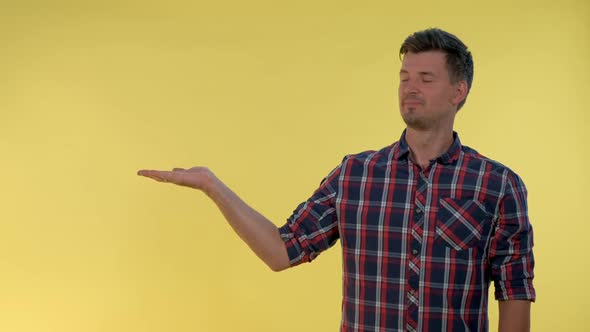 Handsome Man Presenting Something on Empty Hand with Yellow Background. alt