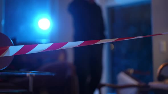 Closeup Red and White Crime Scene Barricade Tape with Blurred Caucasian Policeman with Flashlight alt
