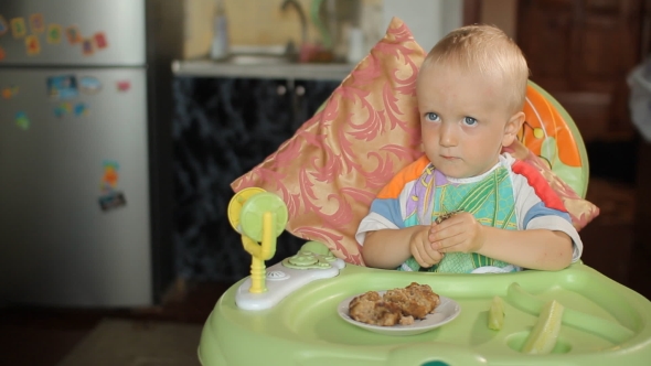 Beautiful Blond Baby Boy Sitting At a Table And Eating Hamburger