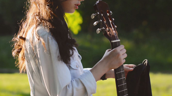 Teen Girl Takes a Guitar out of a Case in the City Park 