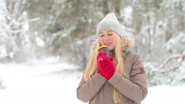 Young happy girl with a cup of coffee in a snowy park alt