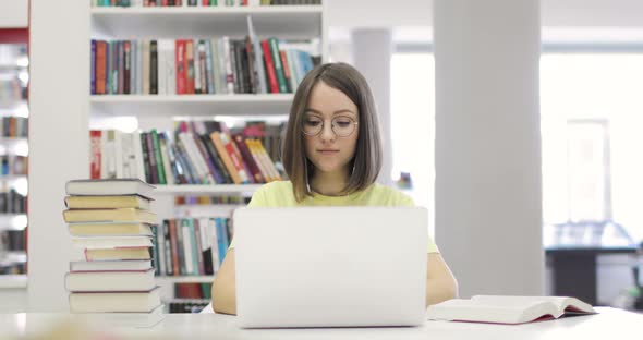 Young Woman is Sitting at a Desk with a Laptop Studying in the Library