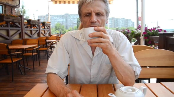 Older Man Sitting At Table And Drinking Tea Outdoors alt