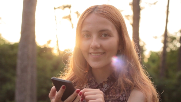 Portrait Of Smiling Happy Girl Using Phone And Looking At Camera