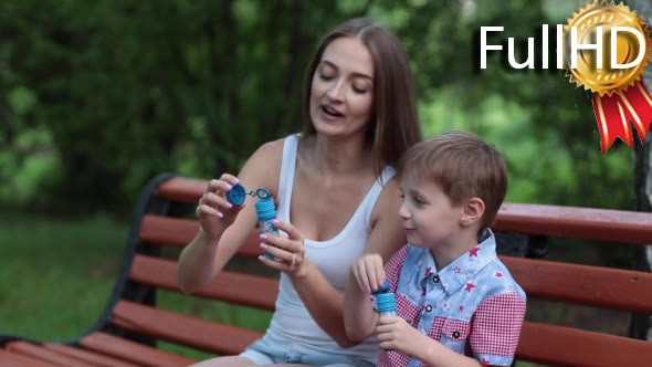 Mother and Son Blow Bubbles Sitting on a Park