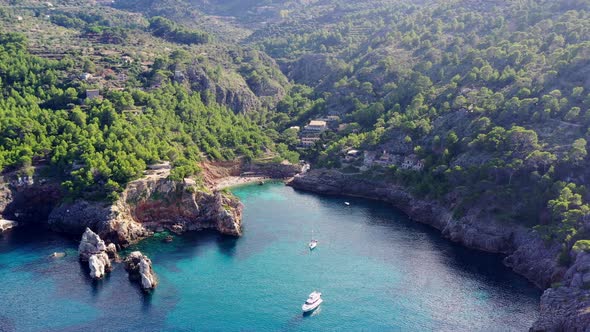 Cala Deia in Mallorca Spain with yacht stationed by the entrance to the cove, Aerial lowering reveal alt