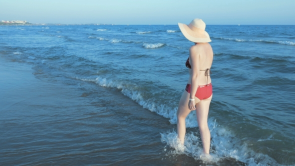 Woman In Bikini With Straw Sun Hat Walking Beach