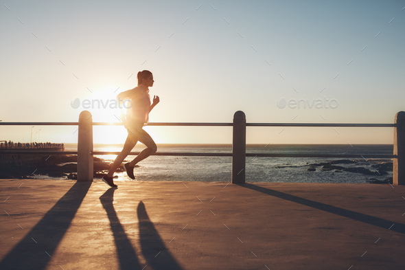 Sportswoman training on seaside promenade at sunset