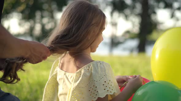 Happy Brunette Girl Playing with Balloons As Male Hands Braiding Long Hair in Sunshine alt