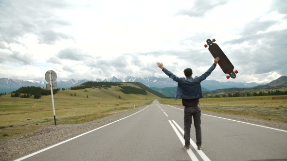 Man Carries a Longboard. The Boy Goes On The Asphalted Road Holding a Longboard alt