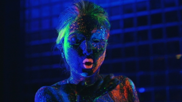 Girl In Ultraviolet Light Blows Pink Fluorescent Powder With Palm alt