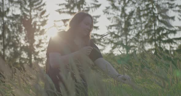 A Girl at Sunset in a Field with Tall Spiky Grass Collects a Field Bouquet alt