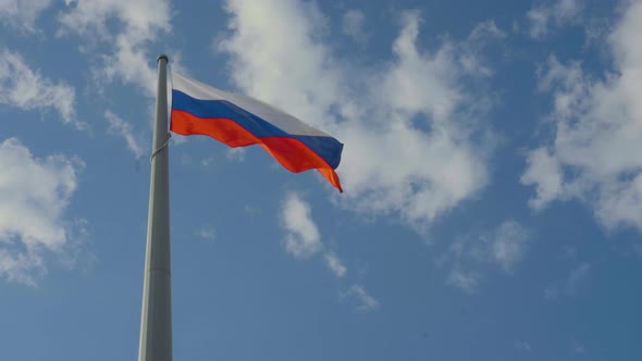 The Flag of Russia Flutters Against a Blue Sky with Clouds