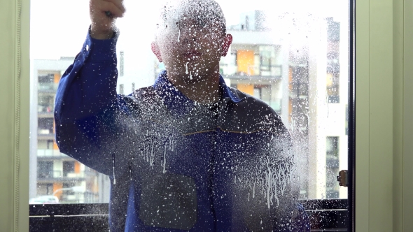 Cleaner Man In Blue Uniform Spray And Wipe Window With Wiper Tool.