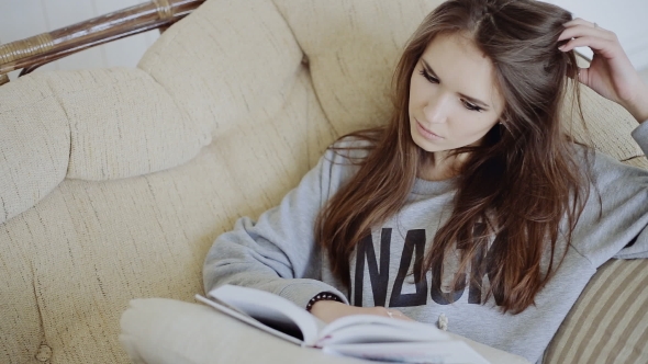 Young Girl Sitting on Chair in Her Living Room Reading Book alt