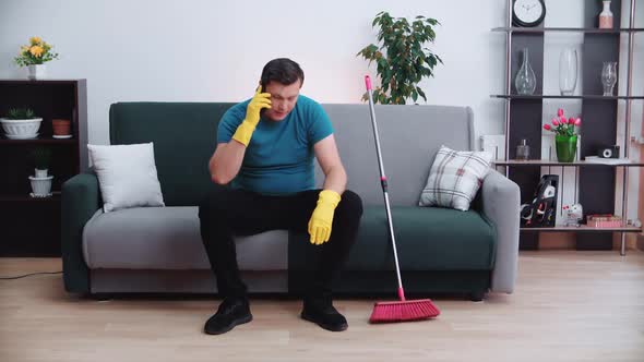 Tired cleaning man sitting on the couch talking on the phone.
