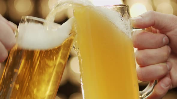 Two friends toast beer mugs spilling beer close-up bokeh background