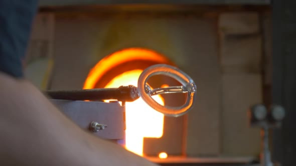 a Man Uses a Steel Tube to Hold Hot Glass Preform