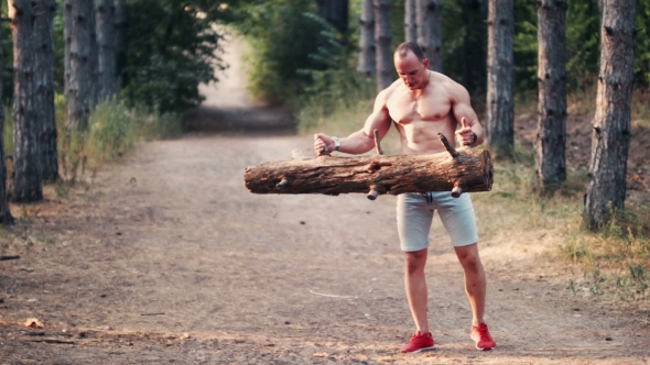 Strong Muscular Man Lifting a Log On a Forest Road alt