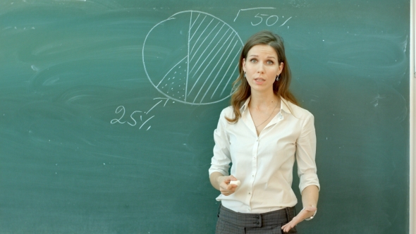 Smiling Female Teacher Holding A Chalk And Writing On The Blackboard Stock Footage