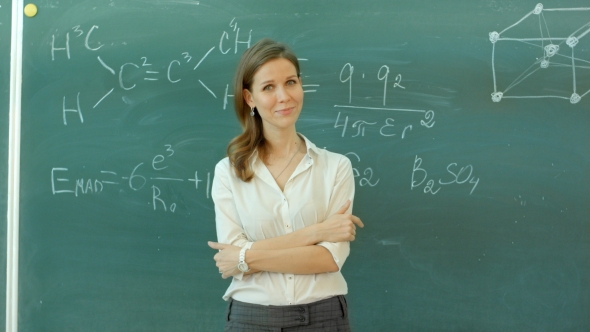 Young Happy Female Teacher With Arms Crossed Standing Against Green Board alt