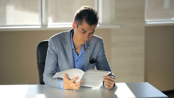 A Young Man In a Suit Jacket Running Notary Flipping Through Documents In Office With a Table On alt